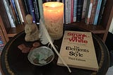 A candle, Buddha figurine, runes, a feather and a book on grammar sit on a table