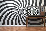 A wall painted with black and white “hypnosis” spirals and an old TV set displaying the same pattern.