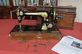 A classic hand-cranked Singer sewing machine in black with a gold decal of a sphinx, and all the attachments.