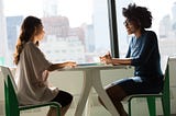 two women sitting beside the table and talking