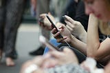 Group of people waiting for the train and looking down, scrolling on their smartphones.
