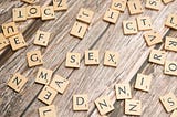 Scattered Scrabble tiles on a table. In the centre of the picture, slightly separate from the other tiles, are the letters S, E, and X.