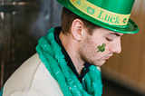 Sad looking man with shamrock sticker on his face wears green hat during Feast of Saint Patrick