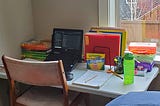 A folding table in a guest bedroom with a laptop, folders, and other school materials arranged on it.
