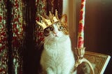 A Siamese cat wearing a golden crown, sitting beside a tall, ornate candle. The cat gazes forward, with wide, expressive eyes, fully aware of its royal status. The vintage aesthetic background adds to the cat’s regal presence.