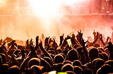 A concert audience with their hands in the air and fog defusing warm lighting