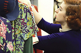 Woman in 1950s clothes looking at a rack of patterned dresses