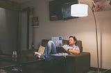 Man sitting on his sofa in a low-lit room with his laptop on.