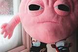 A pink brain with sad eyes and a frown, wearing sneakers and standing on a windowsill.