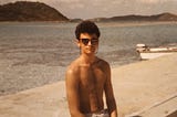 Poet as a teenager sitting on a dock wearing Vuarnet sunglasses at Little Dix Bay