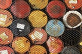 Multi-color oil barrels behind a chainlink fence.