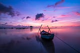 A rowing boat on a calm sea beneath a blue and pink sunrise.
