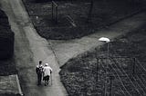 A man walking beside an old woman on a road.