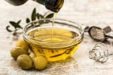 Bowl of olive oil being filled by bottle