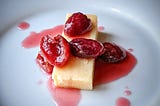 A piece of cheddar cheese with cherries on top and cherry syrup drizzled around the plate