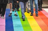 A group of people walking on a road that is painted rainbow colors