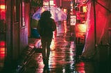 person carrying a translucent umbrella walks down a glowing city street at. night