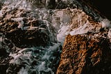 A warm close-up photo of rocks bathed in frothy seawater.