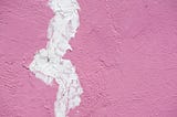 An close up of a wall panted pink with spackle filling in a large crack