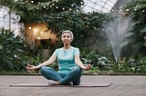 Middle-aged woman with short hair meditating on a yoga mat in a relaxing garden.