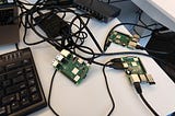 3 Raspberry Pi computers and a mess of cables on a desk next to a keyboard