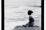 A woman sites on a cliff overlooking Muriwai beach