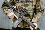 Torso of a paramilitary in standard army attire, holding a semi-automatic rifle across his body.