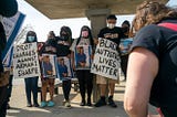 Photo from protest showing 5 African American individuals holding signs and photos. Signs read “Drop Charges Against Armani Sharpe” and “Black Autistic Lives Matter”