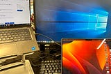 A photo from the office displaying 3 screens: a windows laptop with an extended display on an external monitor, and a macbook.