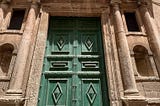 A large, green, ornate door to a baroque Sicilian building