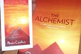 The picture contains a book and a bookmark of The Alchemist. The picture wants to promote reading