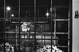 Flowers behind a window of a flower shop with an unlit open sign.