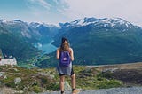 Woman stands at edge of mountain overlooking river in Norway