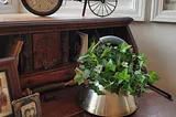 Picture of a burnt tea kettle repurposed as a decorative potholder for green ivy, sitting on a desk.