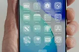 An iPhone screen filled with app icons on the transparent, Liquid Glass user interface.