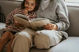 A child cuddles up their mother while she reads a book to her.