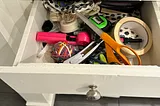 a junk drawer containing, scissors, tape and a rubber band ball amongst other items.