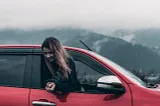 A woman sticking her head and upper body out of a car window.