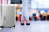 a girls legs standing beside a silver samsonite luggage in an airport