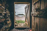 A view of a rugged beach and ocean through a wooden doorway.