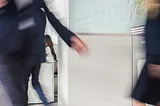 Blurred motion of businesswoman holding documents and walking into a bustling office building.