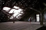 The rooftop scene of the house in the movie Edward Scissorhands — the roof has a hole in it. The room is empty, except for one of the characters in the movie, staring up at the hole.