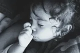 Black and white photo of a toddler, eyes closed, sucking her thumb