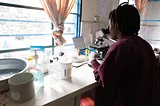 A lab technician in a community clinic, inspects a patient’s culture for signs of infection