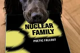 a dog holding a copy of Nuclear Family in its mouth