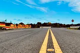 A low-angle view of a straight asphalt road with bright yellow lane lines under a blue sky, symbolizing direction and movement.