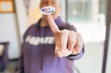 A person with a “I voted” sticker on their finger in the foreground, the person holding the sticker blurred in the background.