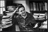 Adrienne Rich sitting in an office, surrounded by books.