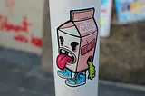 A sticker with a cartoon of a carton of milk with a face sticking its tongue out.