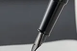 The black fountain pen with its nib resting on a piece of paper.